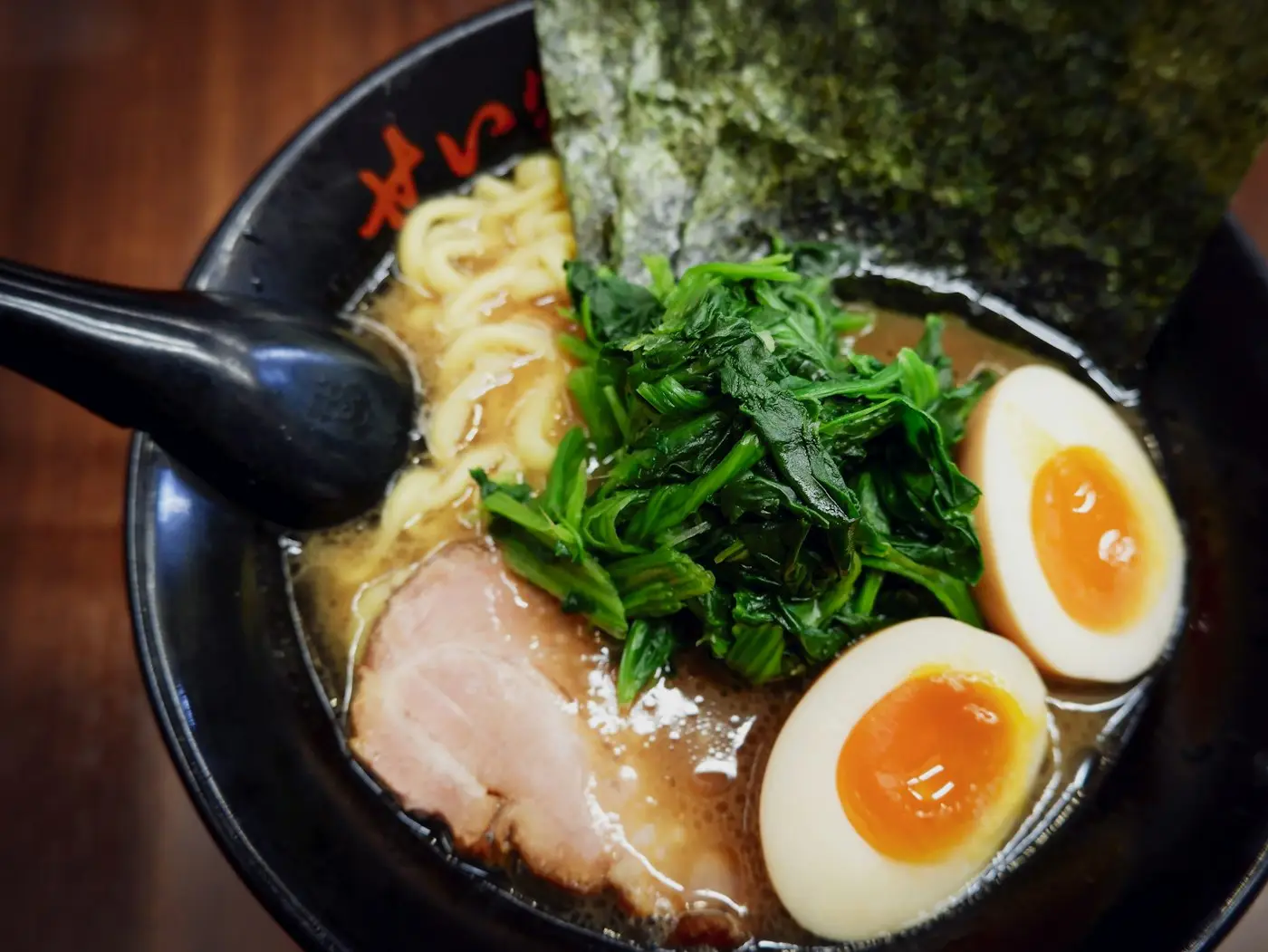 Un bol de ramen au bouillon blanc, œuf mollet et légumes verts
