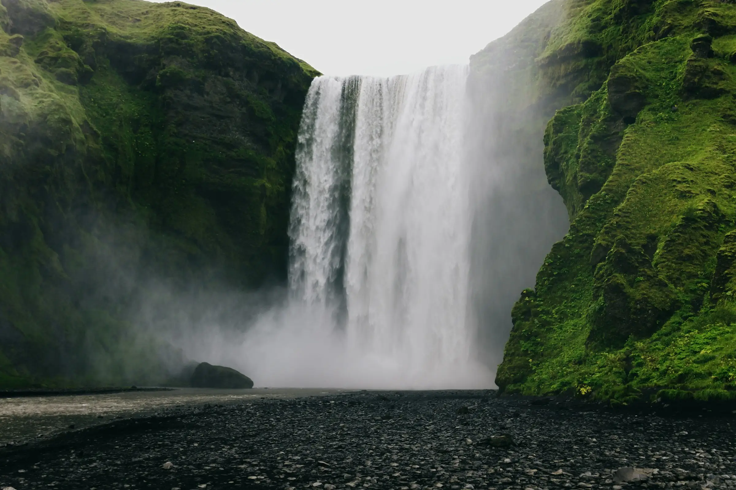 La cascade de Skógafoss tombant d'une falaise verdoyante, en Islande