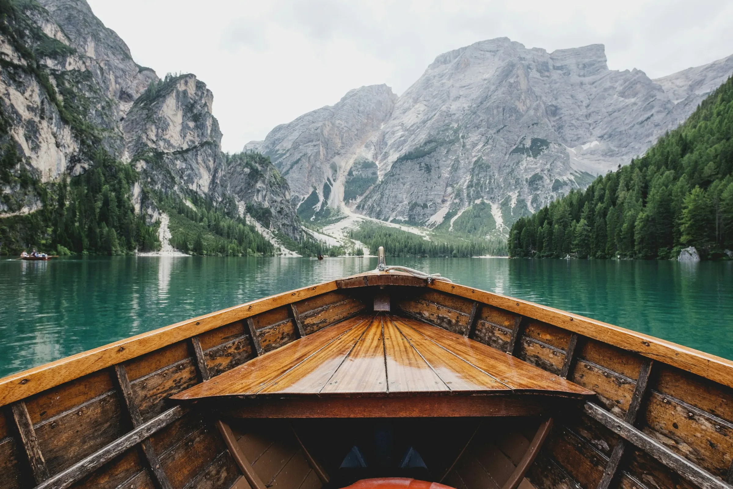 Une barque en bois sur un lac turquoise entouré de montagnes